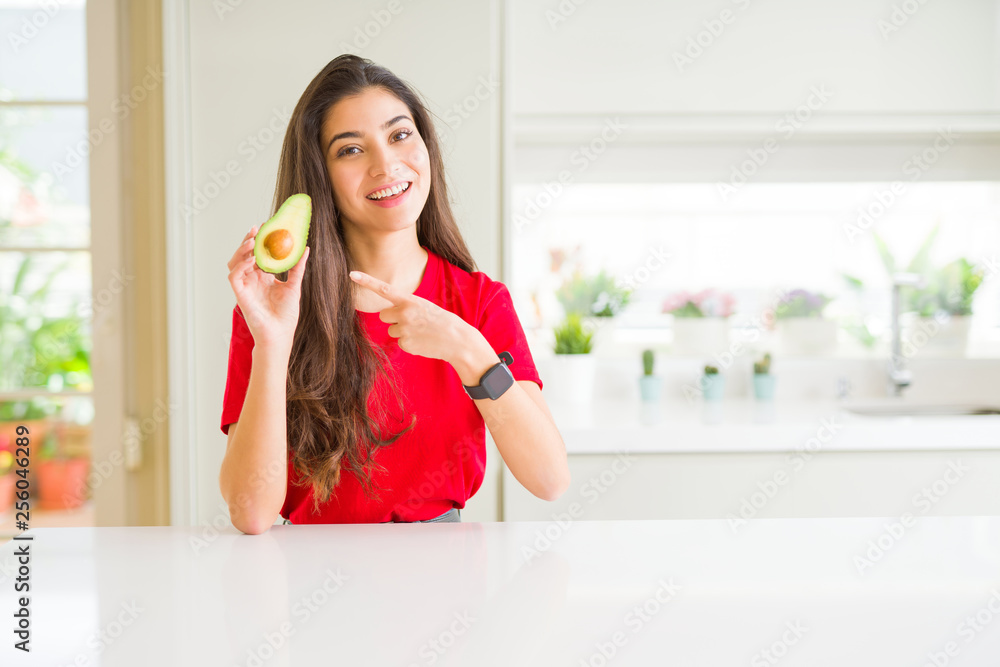 Young woman eating healthy avocado very happy pointing with hand and finger Young woman eating healthy avocado very happy pointing with hand and finger