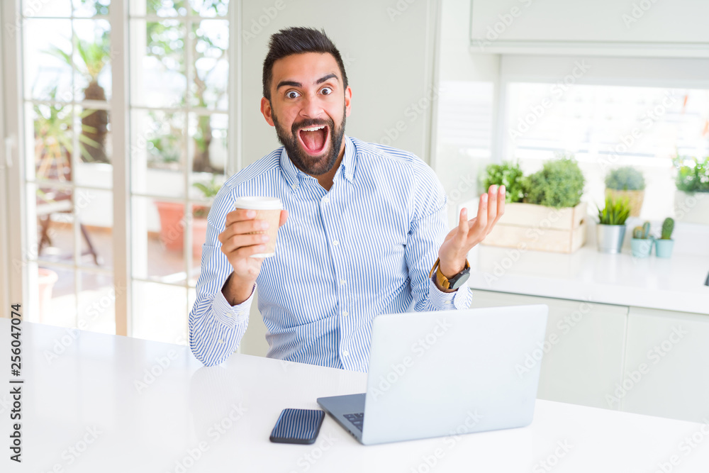 Handsome hispanic man working using computer laptop and drinking a cup of coffee very happy and excited, winner expression celebrating victory screaming with big smile and raised hands