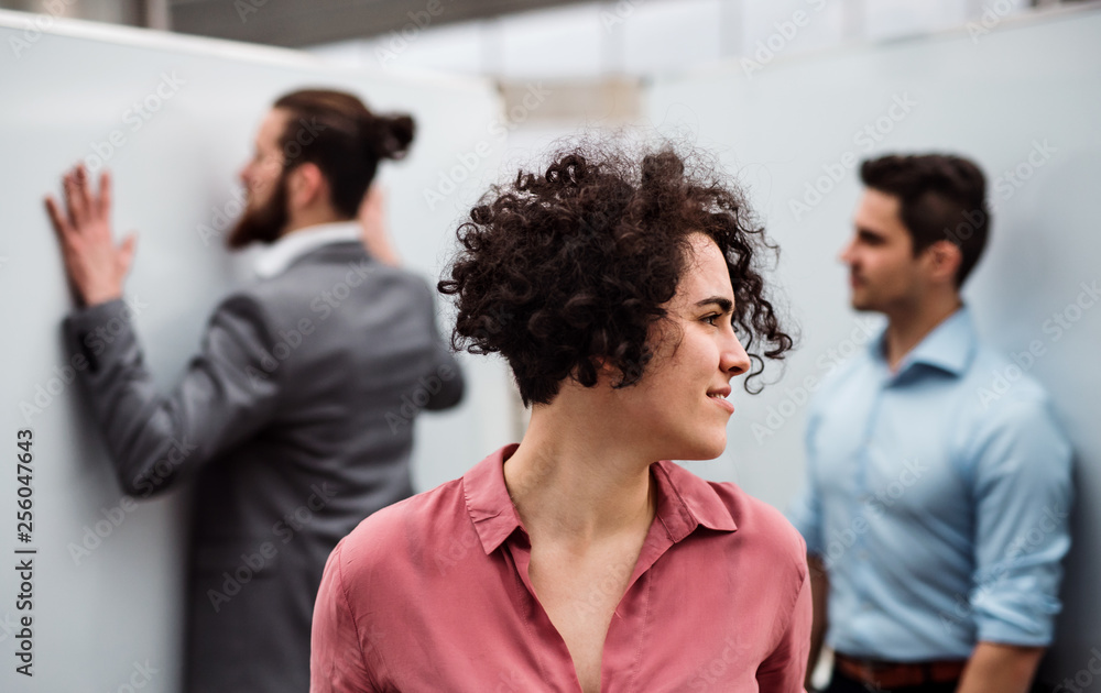 A young businesswoman standing in office, colleagues in the background. A young businesswoman standing in office, colleagues in the background.