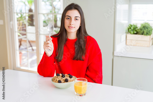 Beautiful young woman having healthy cereals and berries for breakfast with a confident expression on smart face thinking serious