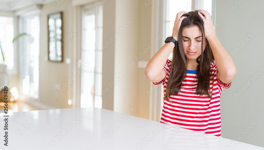 Beautiful young woman wearing casual stripes t-shirt suffering from headache desperate and stressed because pain and migraine. Hands on head. Beautiful young woman wearing casual stripes t-shirt suffering from headache desperate and stressed because pain and migraine. Hands on head.