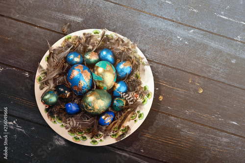 Painted colored Easter eggs on animal skin in plate on dark wooden background. Boho stile.