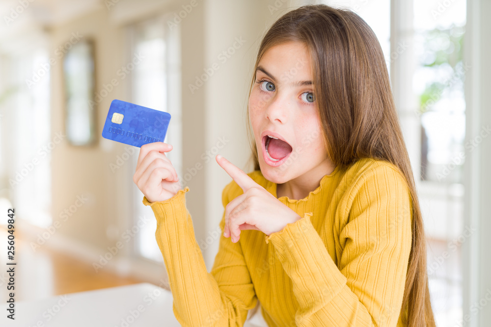 Beautiful young girl kid holding credit card very happy pointing with hand and finger Beautiful young girl kid holding credit card very happy pointing with hand and finger