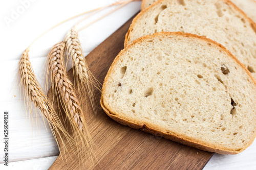 fresh sliced bread and wheat on wooden cutting board on white wooden table, top view