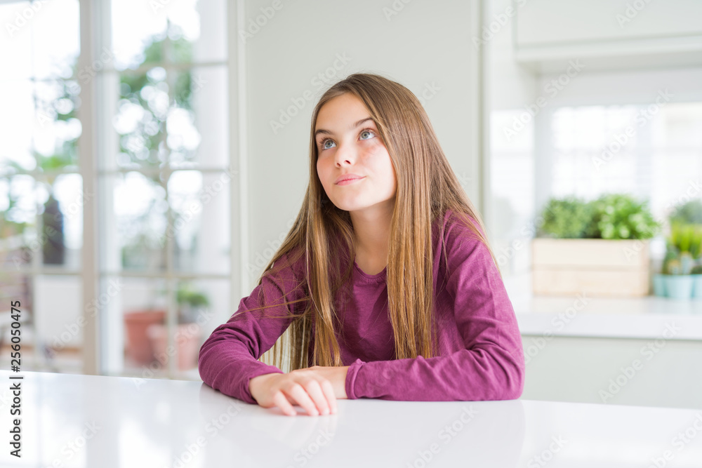 Beautiful young girl kid on white table smiling looking side and staring away thinking.