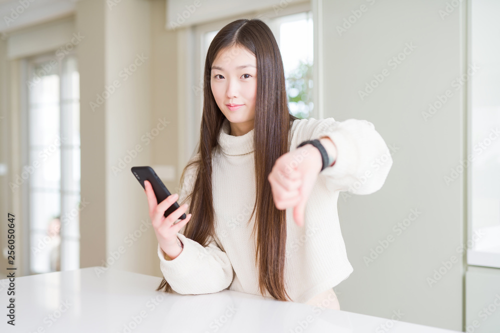 Beautiful Asian woman using smartphone with angry face, negative sign showing dislike with thumbs down, rejection concept Beautiful Asian woman using smartphone with angry face, negative sign showing dislike with thumbs down, rejection concept