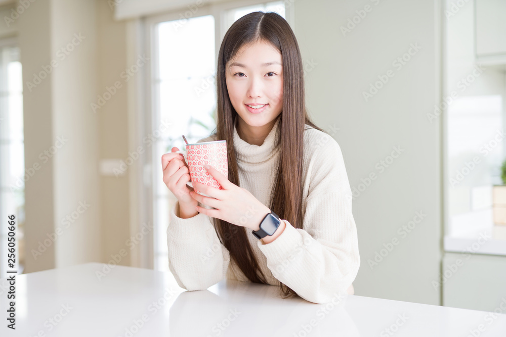 Beautiful Asian woman drinking a cup of coffee with a happy face standing and smiling with a confident smile showing teeth