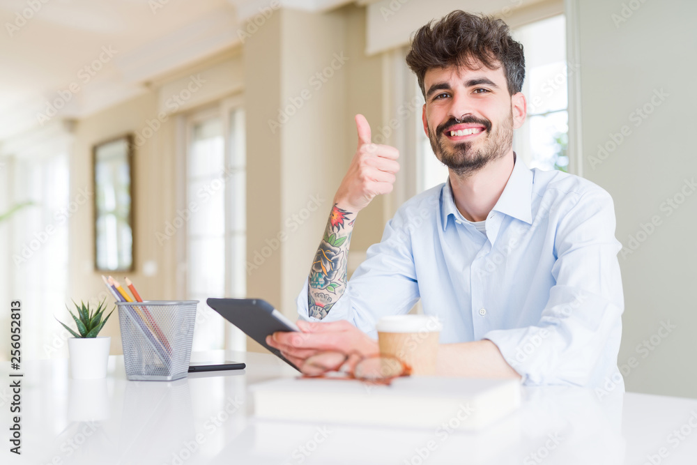 Young business man using touchpad tablet happy with big smile doing ok sign, thumb up with fingers, excellent sign Young business man using touchpad tablet happy with big smile doing ok sign, thumb up with fingers, excellent sign