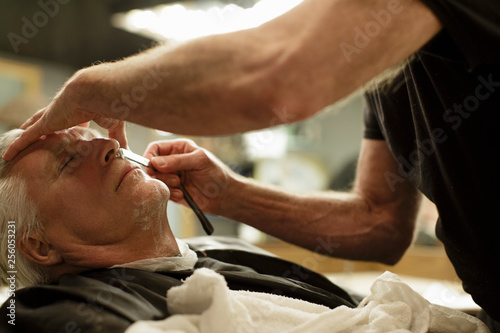 Barber shaves senior man's face with a straight razor photo