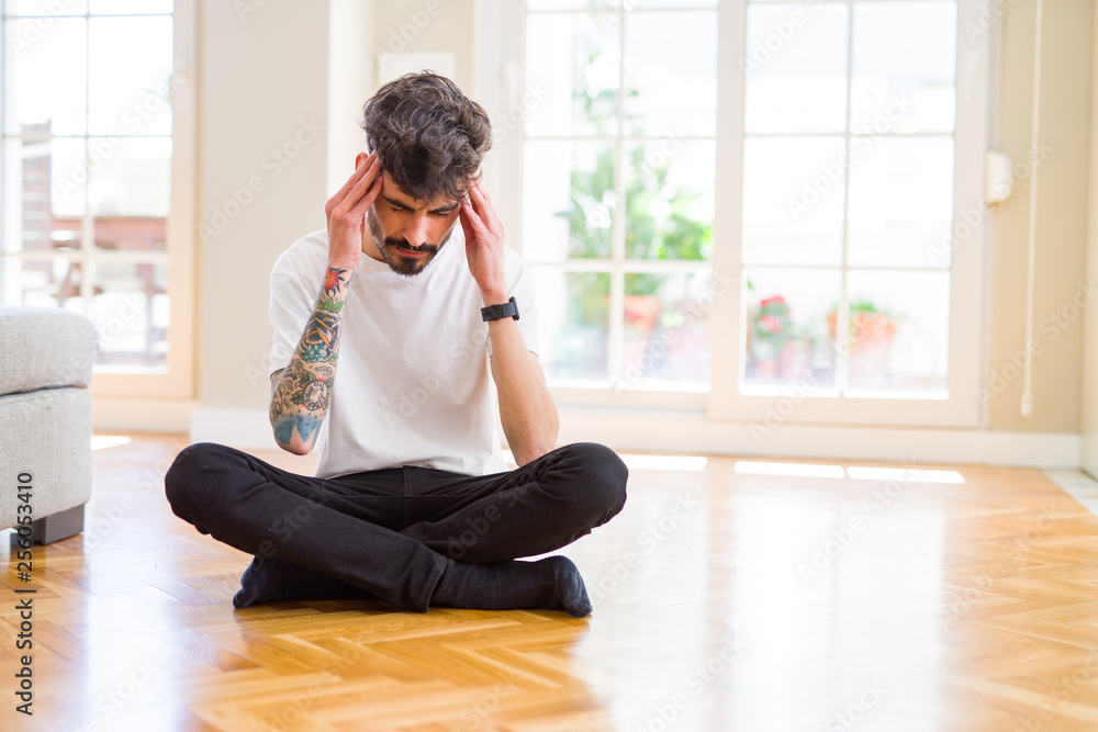 Young man working sitting casual on the floor at home suffering from headache desperate and stressed because pain and migraine. Hands on head.
