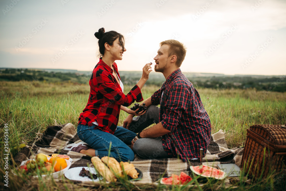 Woman feeds grapes to her man on picnic Woman feeds grapes to her man on picnic