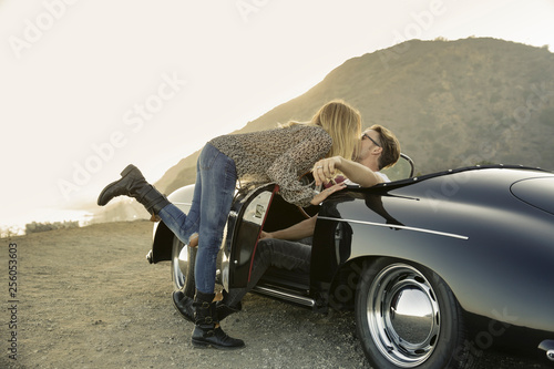 Young woman leans over to kiss young man in convertible