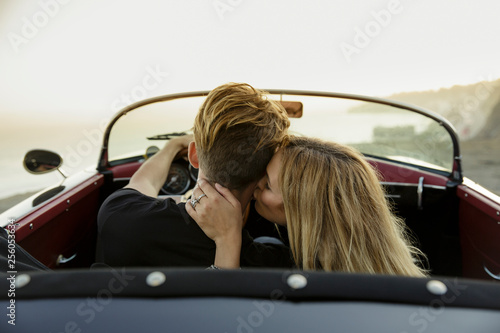 Young woman kisses man's neck while they sit in convertible photo