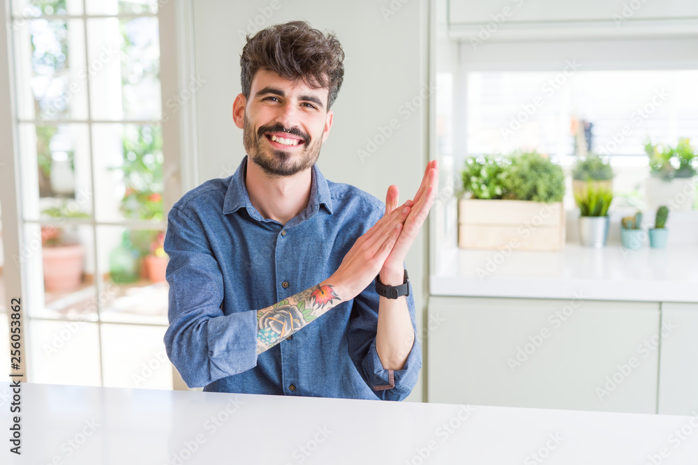 Young man wearing casual shirt sitting on white table Clapping and applauding happy and joyful, smiling proud hands together