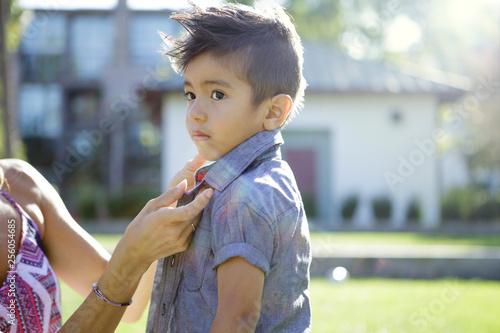 Young boy looks off while mother buttons his shirt