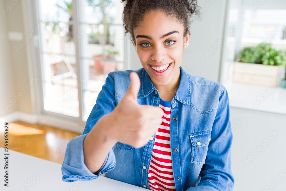 Beautiful young african american woman with afro hair wearing casual denim jacket doing happy thumbs up gesture with hand. Approving expression looking at the camera with showing success. Beautiful young african american woman with afro hair wearing casual denim jacket doing happy thumbs up gesture with hand. Approving expression looking at the camera with showing success.