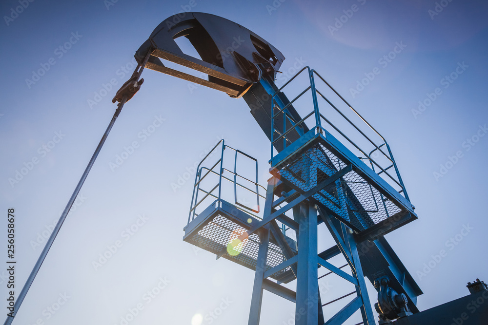 Oil pump on the background of blue sky and the morning sun, sun glare on the oil pump Oil pump on the background of blue sky and the morning sun, sun glare on the oil pump