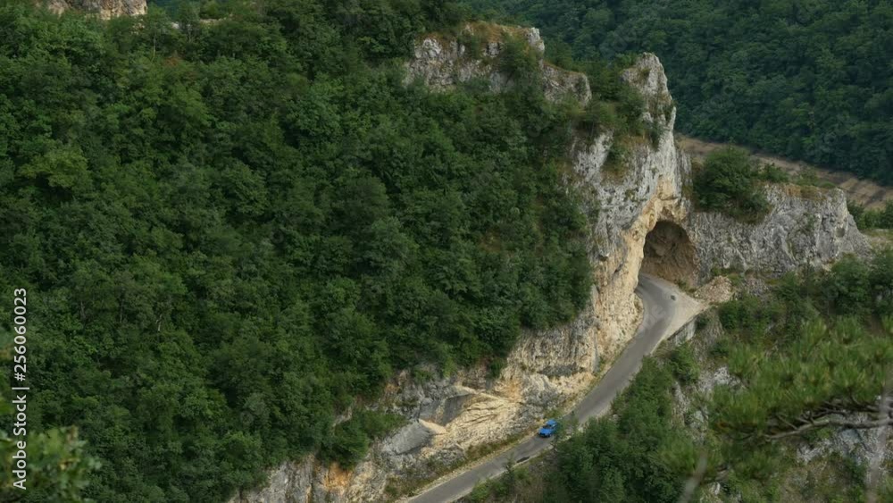 Cars move from tunnel on mountain road. Cars moving on dangerous road. Panoramic shot of mountains road with moving cars Cars move from tunnel on mountain road. Cars moving on dangerous road. Panoramic shot of mountains road with moving cars
