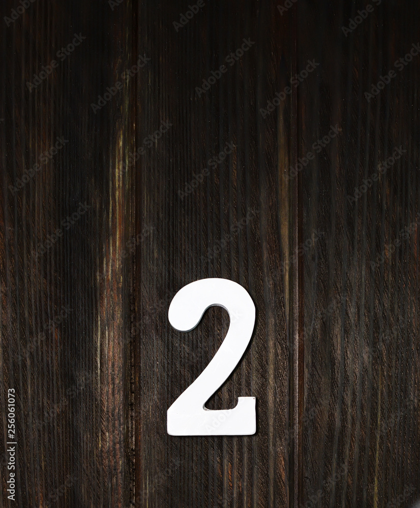 The number 2 is white on a wooden background, dark color board. The number 2 is white on a wooden background, dark color board.