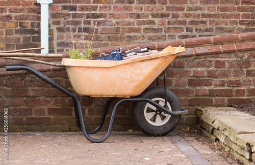 Close-up: Old Orange Garden Carts with Garden Tools and Green Plant are Near Brick Wall. Spring Garden Works. A gardener's cart. Concept: Gardening and Agriculture. photo