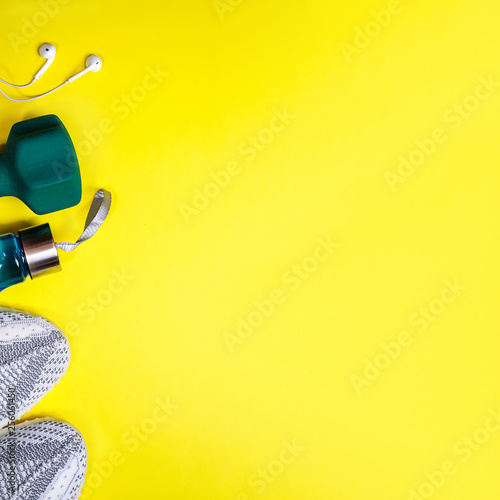 Top view composition with fitness equipment and space for text on bright yellow background. Sport lifestyle concept with sneakers, dumbbell, bottle of water and headphones. Copy space, flat lay