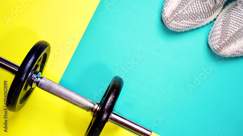 Fitness equipment on yellow and blue color background. Healthy and active lifestyle concept with trendy sneakers, dumbbell. Copy space, flat lay, top view