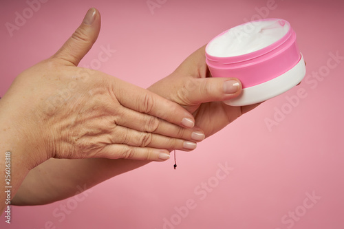 Senior woman hands applying cream on hands on coral background