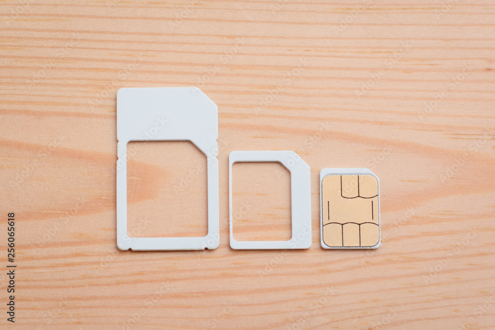 Nano sim card and adapters for different size on wooden table. Choosing right size of a SIM card for mobile phone Nano sim card and adapters for different size on wooden table. Choosing right size of a SIM card for mobile phone