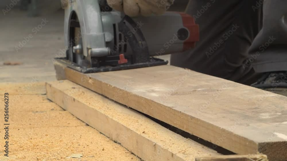 Worker with saw cuts wood Worker in uniform with a circular saw cuts a piece of wood Worker with saw cuts wood Worker in uniform with a circular saw cuts a piece of wood