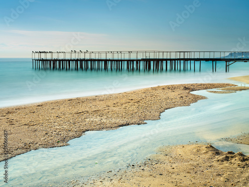 view to golden beach with old metal pier in smooth water