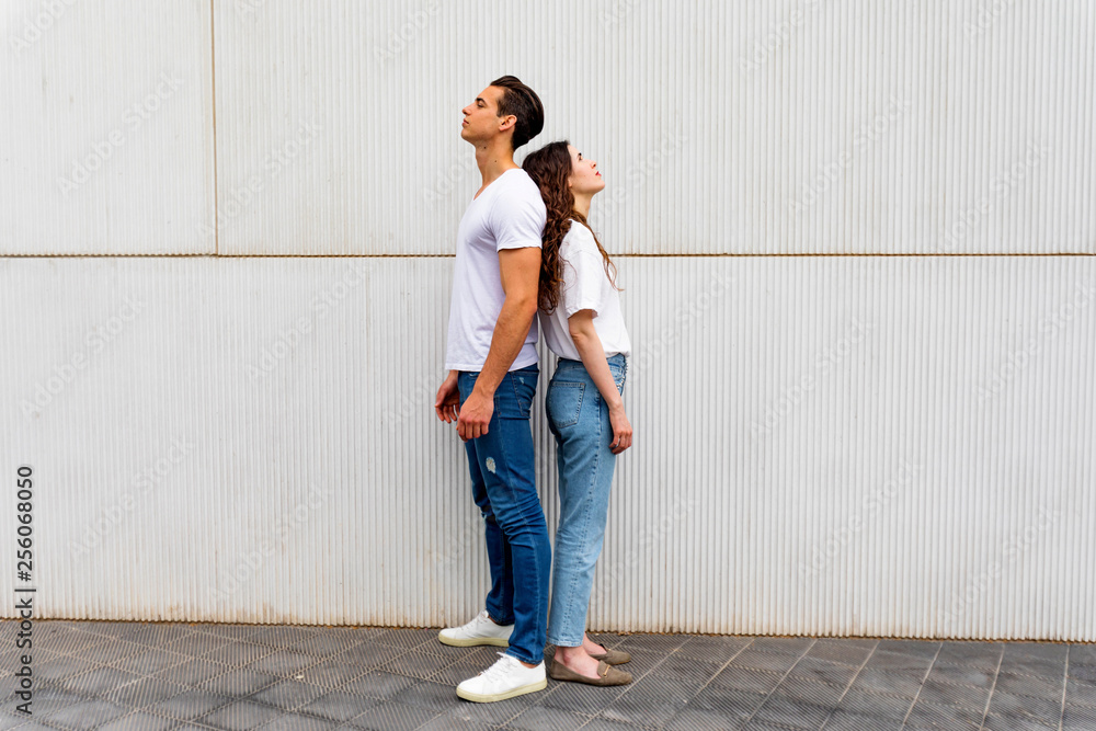 Portrait of unhappy frustrated couple standing back to back not speaking to each other after an argument while standing on grey background