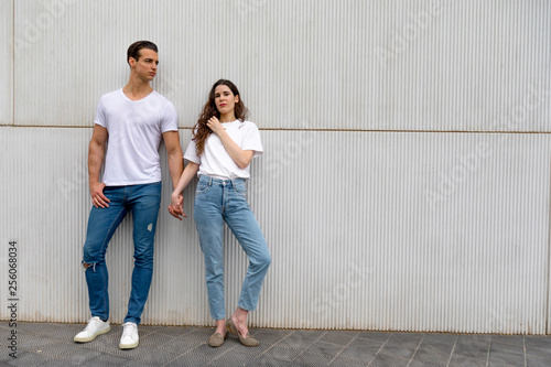 Happy Couple Leaning Against Wall Holding Hands wearing casual clothes in a bright day