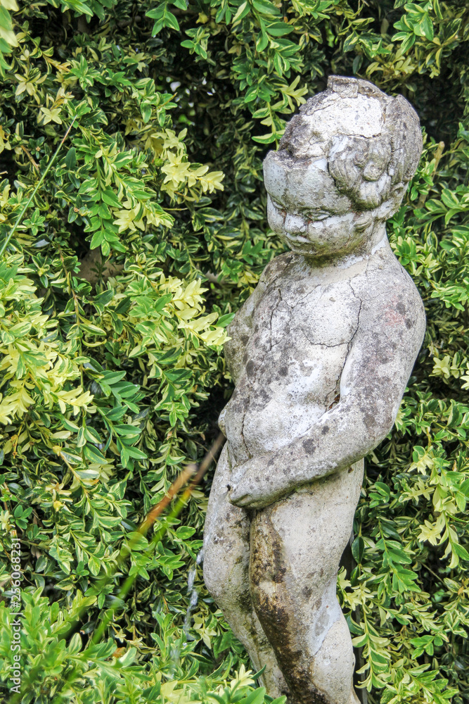 Old statue of a boy standing urine in a garden, which is sunken in oblivion.