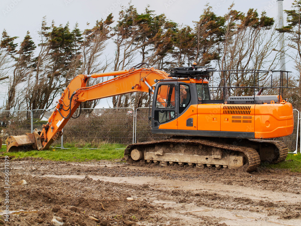 Excavator on a construction site standing by a security fence.