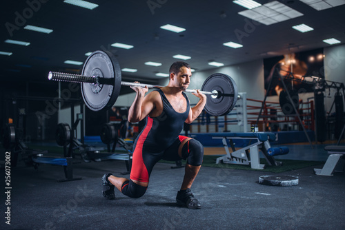 Weight lifter doing squats with a barbell in gym