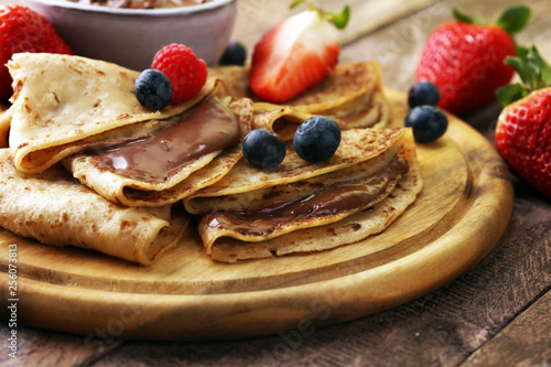 Delicious Tasty Homemade crepes with chocolate or pancakes with raspberries and blueberries on rustic wood