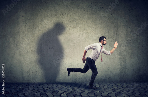 Man running away from his sad gloomy fat shadow on the wall.