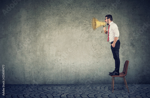 business man standing on a chair and screaming into a megaphone