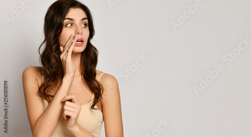 Beautiful young woman looks aside at free text space and holds her arm at mouth like she talks something in a whisper