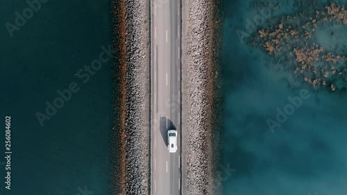 Straight down aerial shot on bridge or rised up road connecting two sides of lake or bay through beautiful blue water. Concept logistics and transportation. Camper van or caravan on travel roadtrip