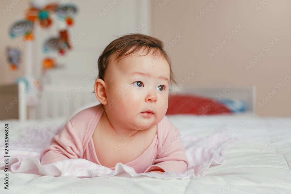 Portrait of cute adorable Asian mixed race baby girl four months old lying on tummy on bed in bedroom. Natural emotion face expression. Window day light. Childhood diversity lifestyle Portrait of cute adorable Asian mixed race baby girl four months old lying on tummy on bed in bedroom. Natural emotion face expression. Window day light. Childhood diversity lifestyle