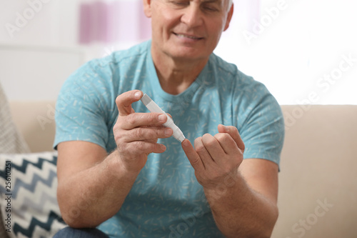 Senior man using lancet pen at home, closeup. Diabetes control