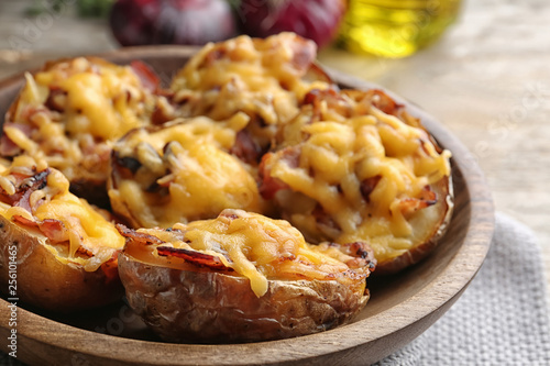 Bowl of baked potatoes with cheese and bacon on table, closeup