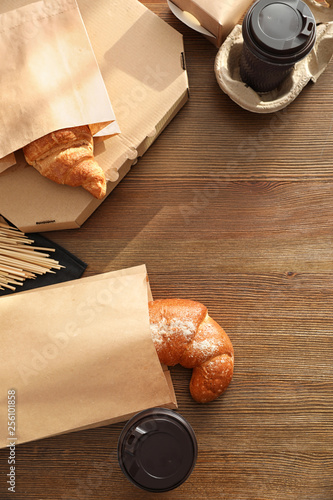 Paper bags with pastry and takeaway food on wooden table, top view. Space for text