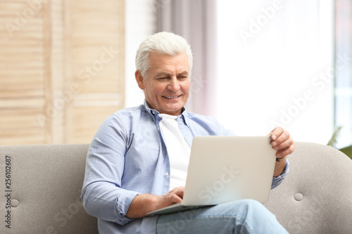 Portrait of mature man with laptop on sofa indoors © New Africa