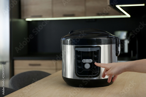 Woman turning on modern electric multi cooker in kitchen, space for text