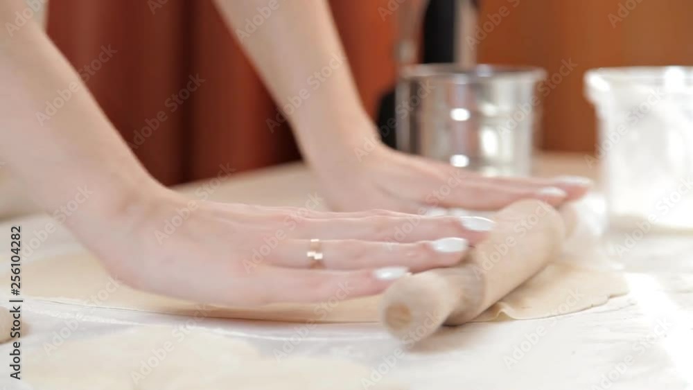 Woman baker rolls the dough with a rolling pin on a background of ingredients on a wooden table and flour Woman baker rolls the dough with a rolling pin on a background of ingredients on a wooden table and flour