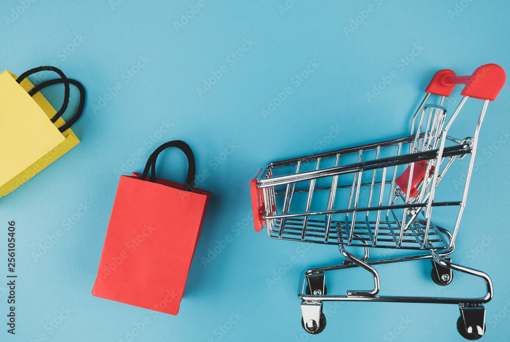 Concept online shopping with shopping cart and paper bag on blue paper background.
