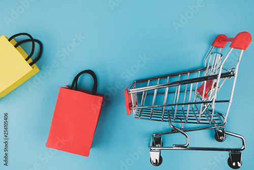 Concept online shopping with shopping cart and paper bag on blue paper background.