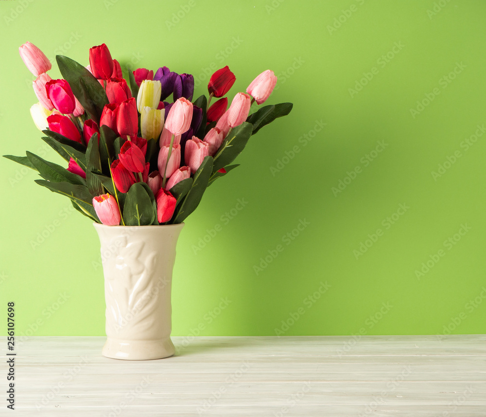 Colorful tulips in vase on white table wall green background Colorful tulips in vase on white table wall green background